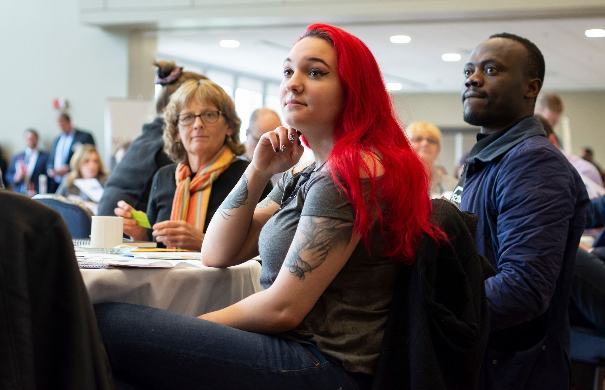 Attendees seated at round tables in a function room, turned toward the front